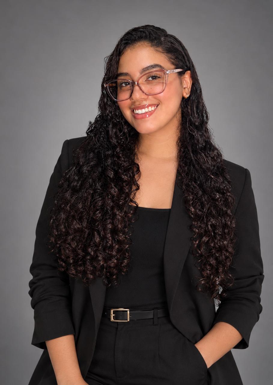 Retrato de Julienne Sáez con blazer negro, sonriendo, sobre fondo gris